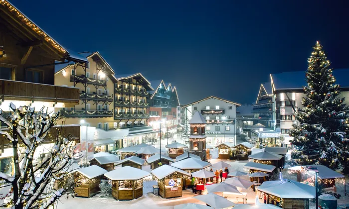 Snow-covered Christmas market with festive lights in alpine village at night